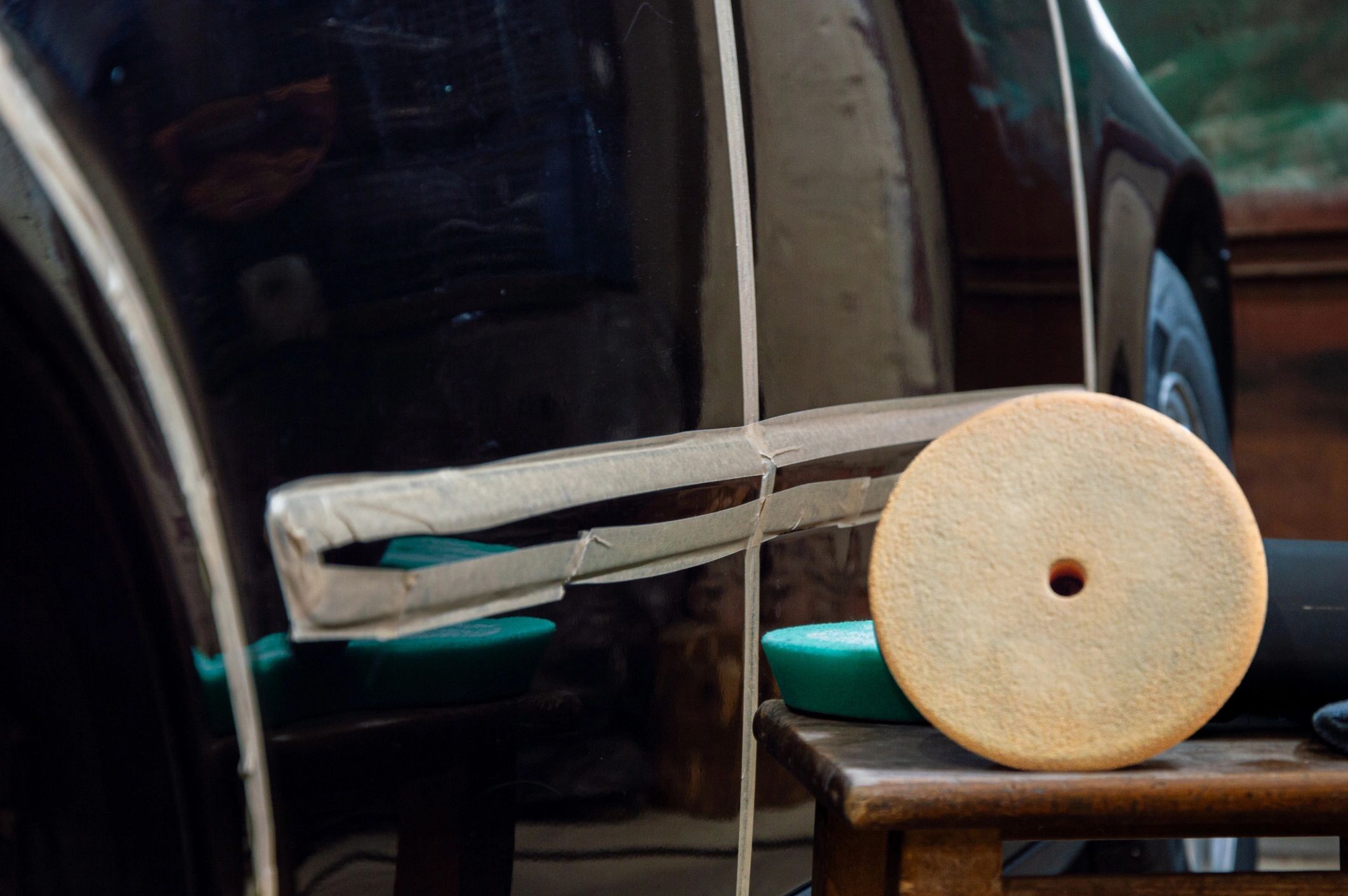 Technician polishing a vehicle surface with a buffer in a workshop